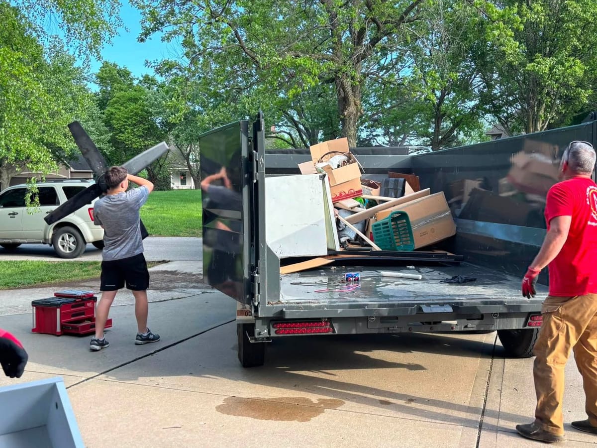 A Plus crew carrying ceiling fan blades and loading a dump trailer in a driveway
