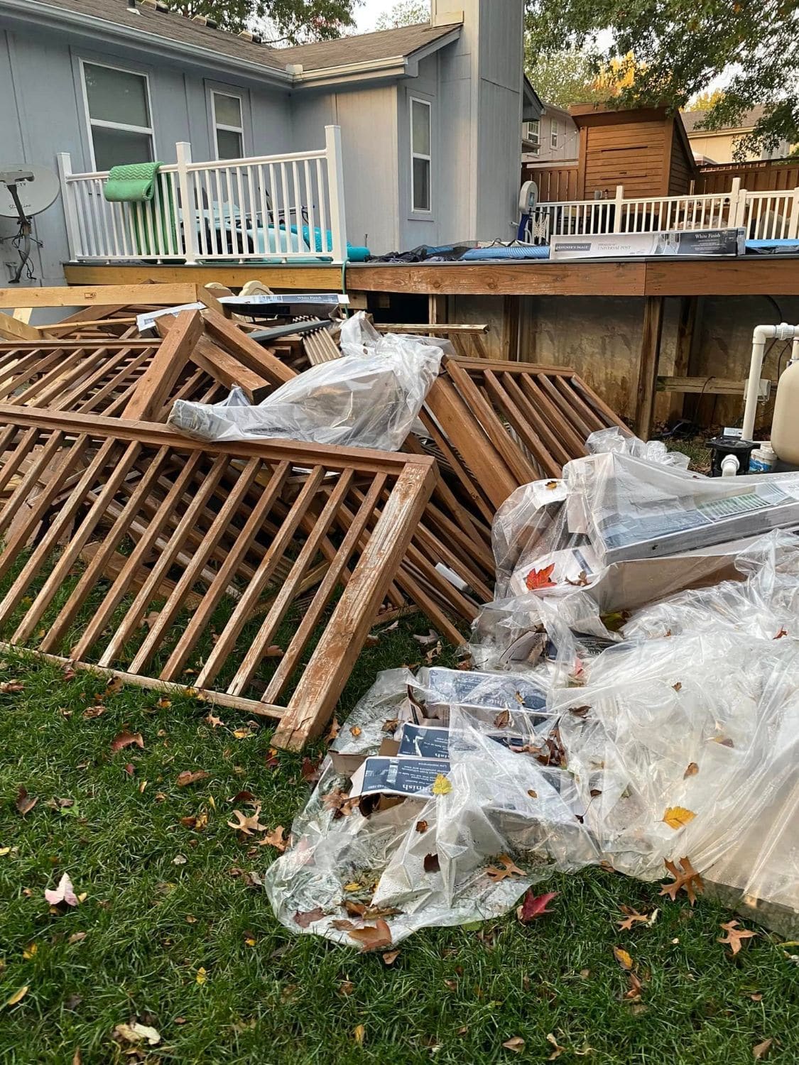 Old wood deck railings and plastic packaging piled on the lawn beside a deck