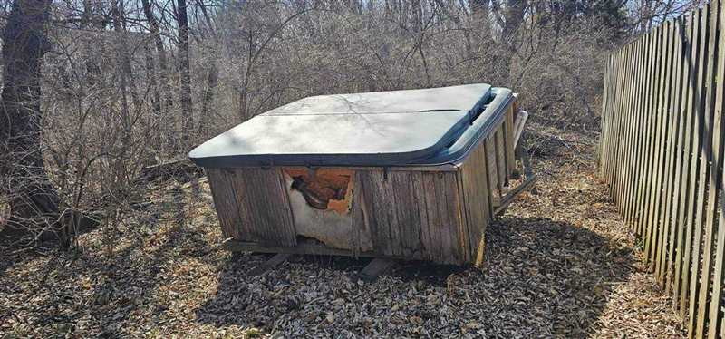 Old weathered hot tub beside a wooden fence before removal in Independence, MO